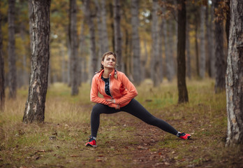 Young attractive sport woman in sportswear doing stretching exercise for hand in autumn forest. Warm up before jogging. Healthy lifestyle concept