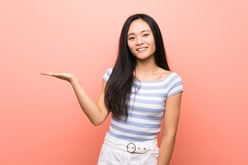 Teenager asian girl over isolated pink background holding copyspace imaginary on the palm to insert an ad