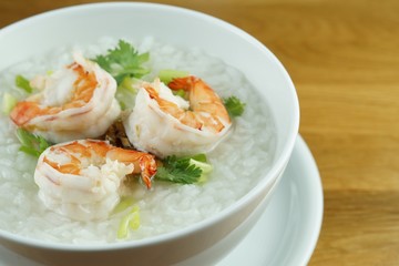 Fototapeta na wymiar Traditional Thai porridge rice gruel and shrimp in a bowl with steaming on wooden table 