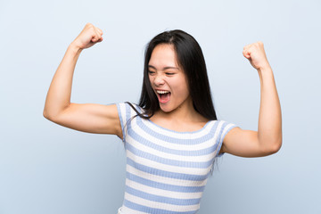 Teenager asian girl over isolated blue background celebrating a victory