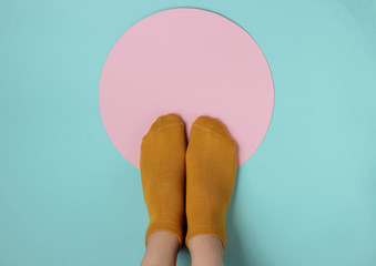 Female slim legs in orange socks on a blue background with a pink circle in the middle. Creative fashion concept, minimalism. Top view