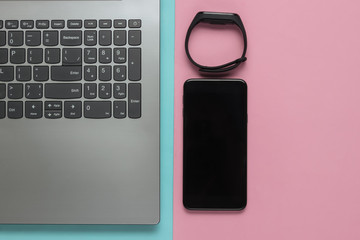 Laptop, smart bracelet and smartphone on a blue-pink pastel background. Modern gadgets. Top view. Flat lay