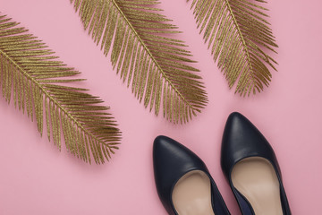 Minimalistic fashion still life. Classic heeled shoes with golden palm leaves on pink pastel...