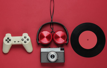 Pop culture media attributes on a red background. Gamepad, film camera, vinyl record, headphones on...