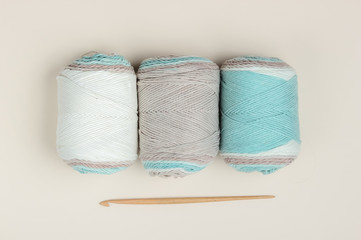 Woolen skeins of thread and crochet hook on a beige background. Top view