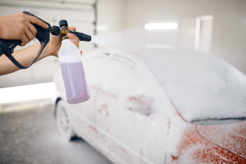 Female washer applies foam to automobile, car wash