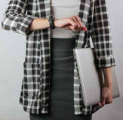 Business business woman in formal clothes holds a laptop and looks at her watch while standing on a white background. Crop photo. Office worker