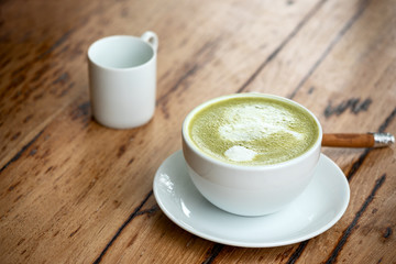 Green tea or hot matcha latte in white ceramic cup with saucer placing together with syrub cup and cinnamon on retro wooden table