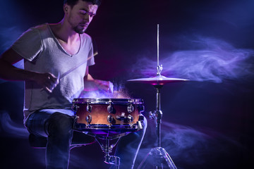 A drummer plays drums on a blue background. Beautiful special effects of light and smoke. The process of playing a musical instrument.