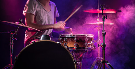 The drummer plays the drums. Beautiful blue and red background, with rays of light. Beautiful special effects smoke and lighting. The process of playing a musical instrument. Close-up photo.
