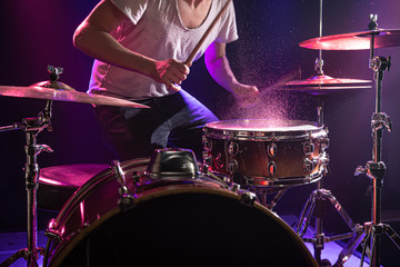 Fototapeta na wymiar The drummer plays the drums. Beautiful blue and red background, with rays of light. Beautiful special effects smoke and lighting. The process of playing a musical instrument. Close-up photo.