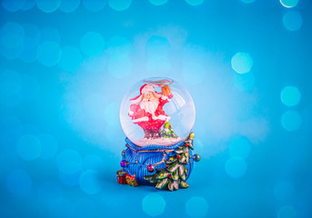 Festive glass sphere inside with Santa Claus on a sparkling blue background. Copy space.