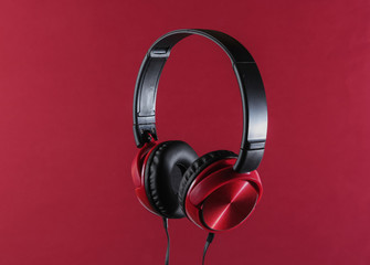 New headphones with cable. Minimalist photo of earphones on red background. Black red dj headphones