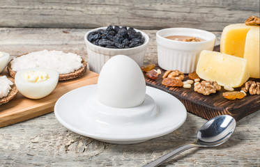 Boiled egg in egg cup and sandwich with cheese with slice egg, raisin, honey, parmesan, nut and pumpkin seed. Healthy breakfast on a wooden table