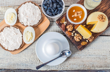 Boiled egg in egg cup and sandwich with cheese with slice egg, raisin, honey, parmesan, nut and pumpkin seed. Healthy breakfast on a wooden table
