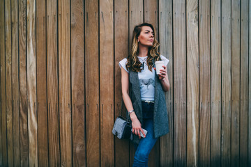 Young attractive hipster girl posing for camera while strolling outdoors near to promotional background.Charming woman standing against wall with copy space for your advertising content outside