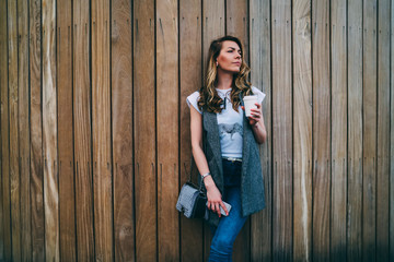 Obraz premium Young attractive hipster girl posing for camera while strolling outdoors near to promotional background.Charming woman standing against wall with copy space for your advertising content outside