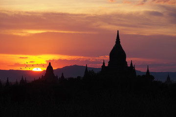 Obraz premium Beautiful silhouette view of the old pagodas and Buddhist temples in Bagan Myanmar during sunset time with dark colorful and warm sky and mountain background. Religious landmark for tourism in Asia