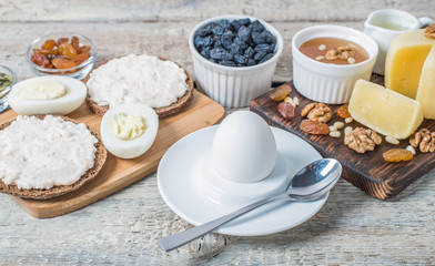 Boiled egg in egg cup and sandwich with cheese with slice egg, raisin, honey, parmesan, nut and pumpkin seed. Healthy breakfast on a wooden table