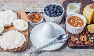 Boiled egg in egg cup and sandwich with cheese with slice egg, raisin, honey, parmesan, nut and pumpkin seed. Healthy breakfast on a wooden table