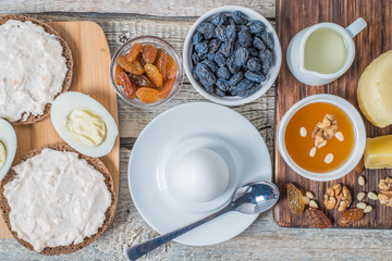 Boiled egg in egg cup and sandwich with cheese with slice egg, raisin, honey, parmesan, nut and pumpkin seed. Healthy breakfast on a wooden table