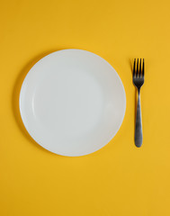 Empty plate with a fork on a yellow background. Studio shot. Restaurant food concept.