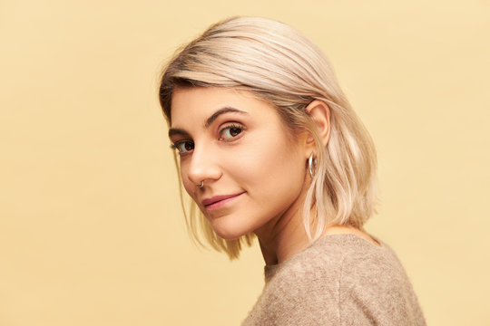 Beauty, style and fashion concept. Attractive twenty year old female with nose ring and dyed bob hair posing isolated looking at camera with enigmatic alluring smile, dressed in cashmere sweater