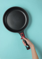 Female hand holds a non-stick pan on blue background. Top view