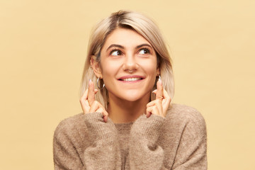 Body language. Portrait of adorable cute young superstitious female with blonde hair and nose ring crossing fingers for good luck, wishing to win in lottery, her eyes full of hope and impatience