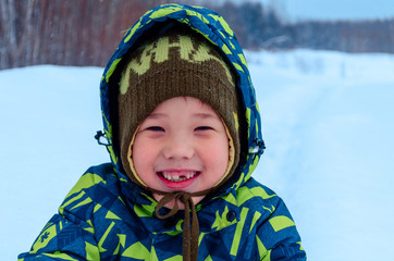 Cute Asian little child boy a green colorful jumpsuit  portrait  smiling on a  white fluffy snow in Siberia. Happy baby playing in the park outdoors in snow on cold winter day. With a smile of happy