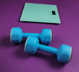 Floor scales and dumbbell on purple background. Sport concept, fitness training. Studio shot