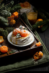 Fototapeta na wymiar Tangerine Pavlova. Famous delicious dessert of meringue, cream and fruit. Christmas look with tangerines on the background of the Christmas tree