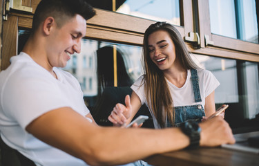 Happy couple in love checking notification for cellphone application during blogging time, positive Caucasian male and female hipster guys communicating about publication text from social networks