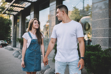 Positive male and female hipster guys holding each other on hands and walking around urban setting...