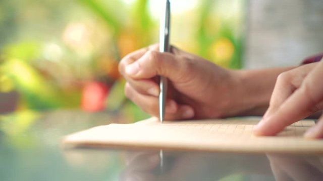 4K video copy space of  man hand writing down in white notebook with bokeh light in cafe background.