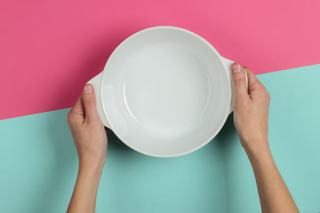 Female hands hold empty ceramic bowl pink blue background. Top view