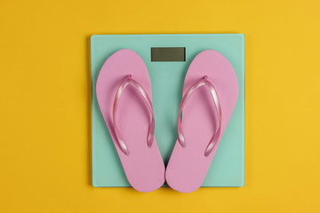 Flip flops on the scales. Studio shot on yellow background. Slimming concept. Top view