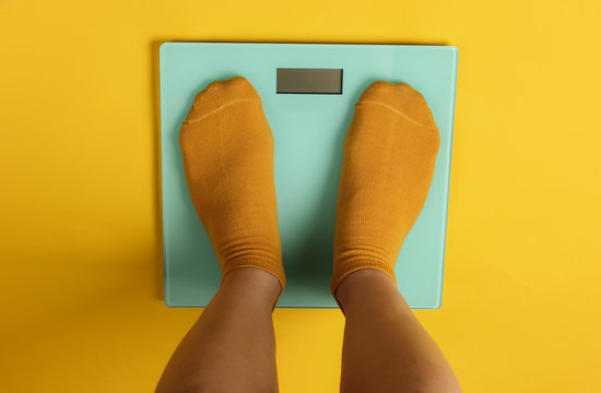 Female legs in socks are standing on the floor scales against yellow background. Top view