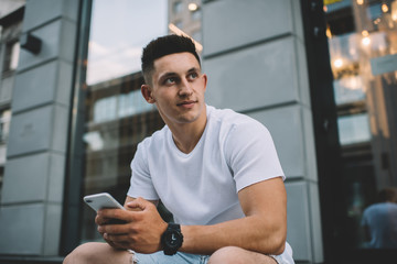 Fototapeta na wymiar Contemplative Caucasian man in casual wear pondering on content text for publication thinking on interesting useful ideas, handsome pensive hipster guy using 4g internet on modern smartphone