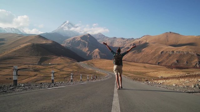 Young caucasian male tourist funny walking to mountains on road slow motion