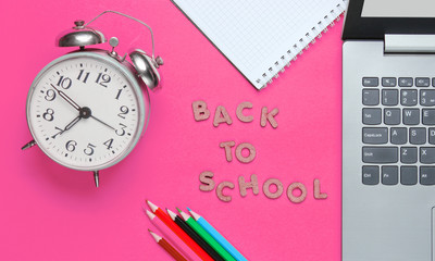 Scholl time minimalistic concept. Laptop, color pencils, notebook, alarm clock on pink background....
