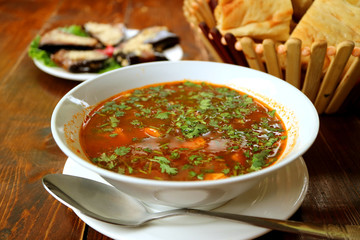 Closeup Hot Georgian Beef Soup Khashi with Blurry Bread and Eggplant Rolls in the Backdrop