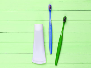 Two toothbrushes with a tube of toothpaste on green wooden background. Top view