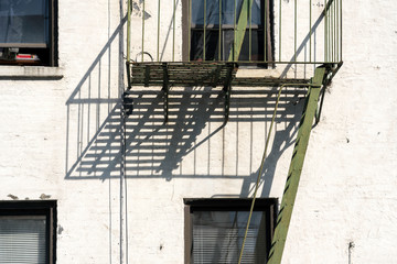Fototapeta na wymiar New York City apartment building with strong shadows cast by fire escape. Typical New York City apartment building but with strong shadows and lines making for a simple graphic image.