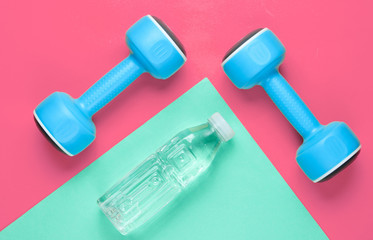 Minimalistic sport concept. Blue plastic dumbbells, bottle of water on colored paper background. Top view