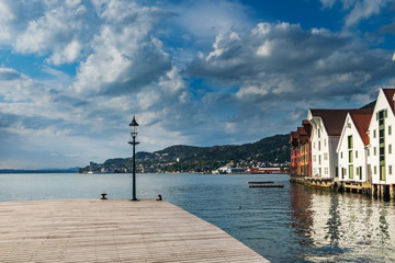 Historical red and white buildings in Bryggen - Hanseatic wharf in Bergen, Norway. Scenic summer panoramic view of the Old Town pier architecture, beautiful waters of Byfjorden and cloudy blue sky