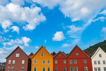 Historical white, red, brown, and yellow buildings in Bryggen - Hanseatic wharf in Bergen, Norway. Scenic summer panoramic view of the Old Town pier architecture under cloudy blue sky