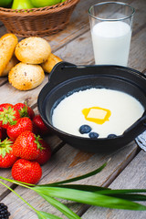 Traditional breakfast milk porridge with butter and berries on a wooden table.