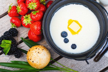Traditional breakfast milk porridge with butter and berries on a wooden table.