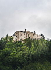 Fototapeta na wymiar Hohenwerfen Castle is a medieval rock Alpine castle and history museum near Salzburg, Austrian Alps, Austria. It is surrounded by pine forests. Castle view on a rainy summer evening at sunset